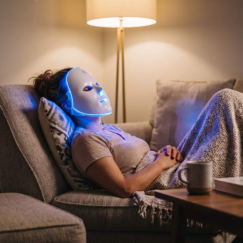 Mujer recostada en el sillón con la máscara encendida en azul y una manta encima