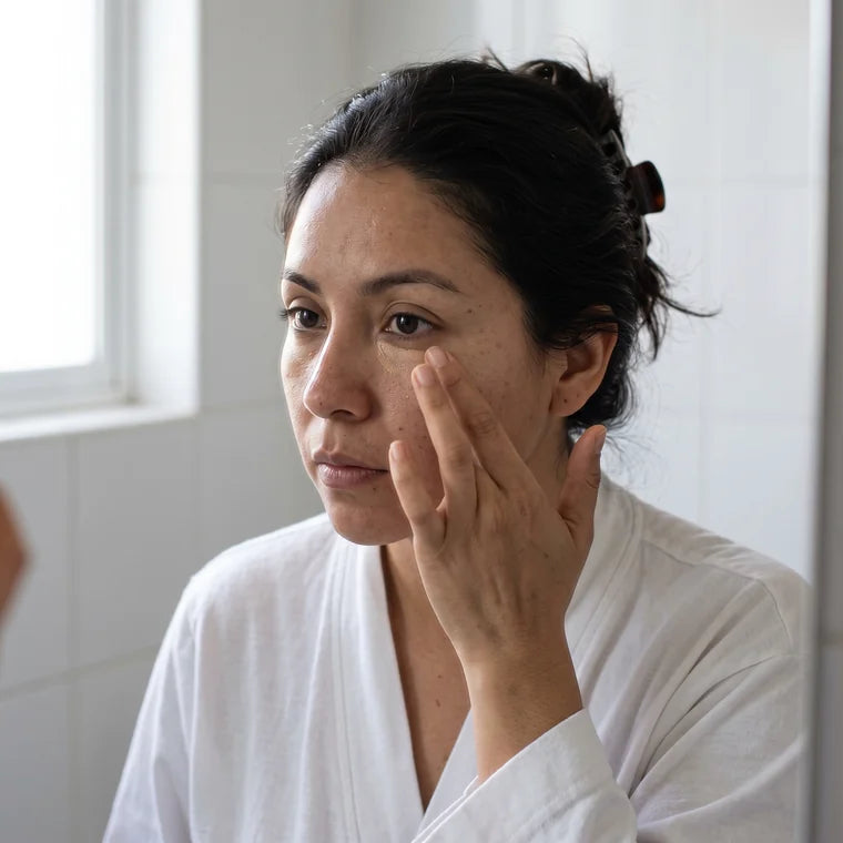 Mujer frente al espejo por la mañana difuminando el corrector bajo el ojo con el dedo anular