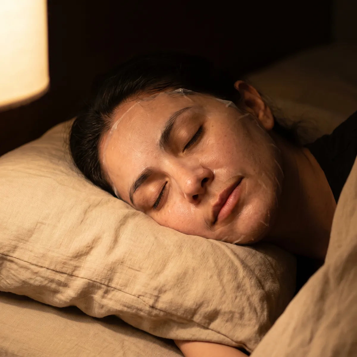 Mujer dormida de lado con la película de la mascarilla ya seca sobre el rostro